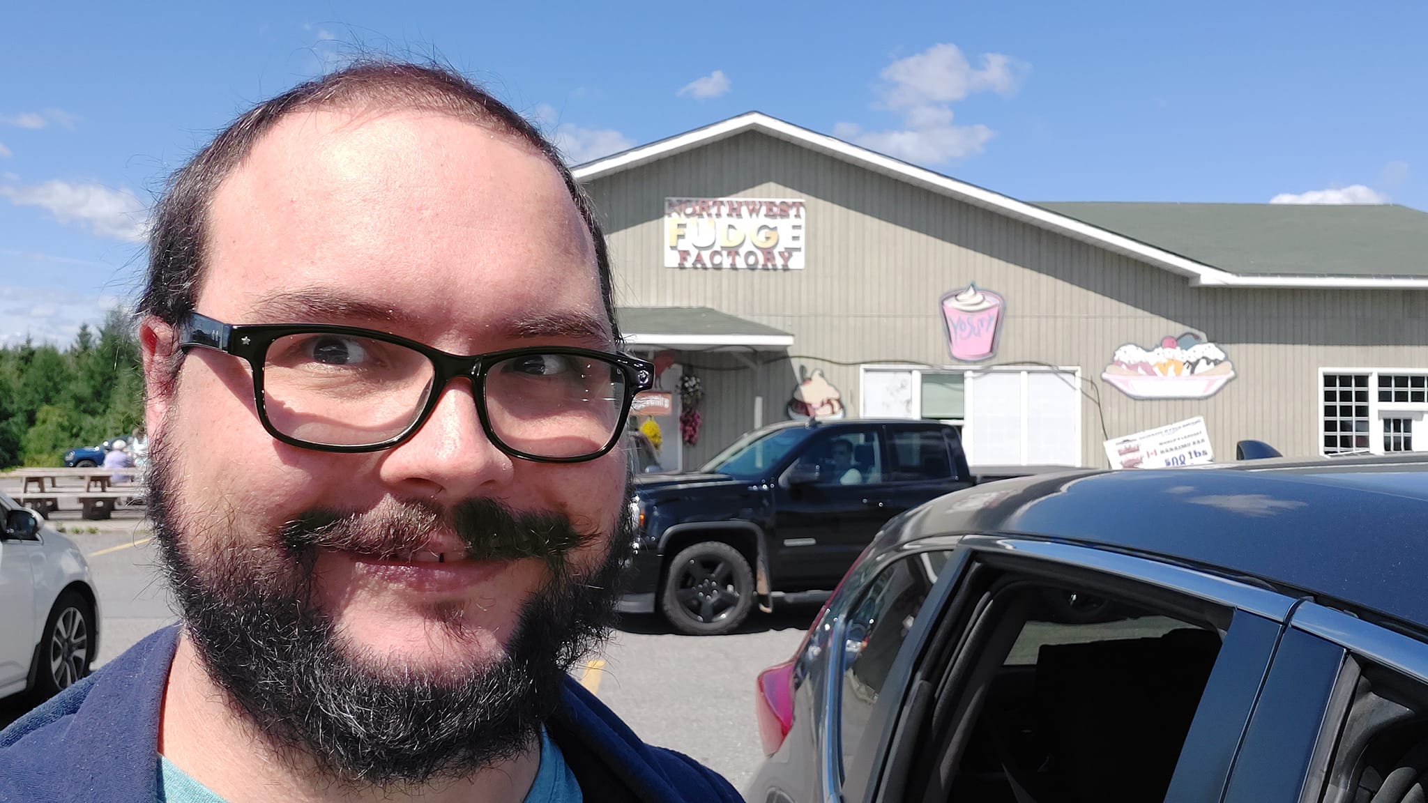 A man short hair and facial hair stands in front of a building with a sign that says Northwest Fudge Factory